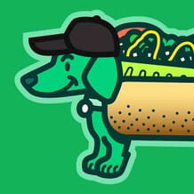 A smiling green dog wears a Chicago Dog costume while wearing a black baseball cap.